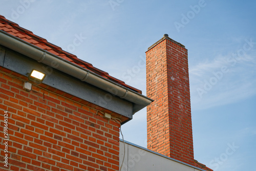 Red brick chimney and roof with gutter against clear blue sky