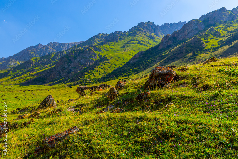 Fototapeta premium Sunlit mountain slope with rocks under clear blue sky
