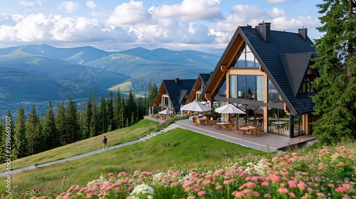 Modern mountain lodges with expansive windows overlook a scenic valley.