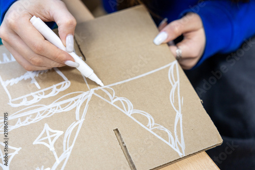 Teen girl's hands, child decorating, painting gingerbread house made from cardboard. Christmas preparation. Concept of eco holiday, New year eve, family, motherhood and childhood