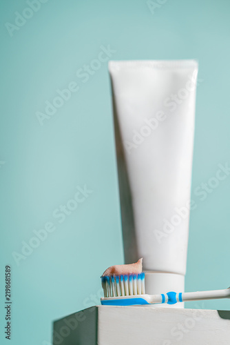 Obraz na plátně A toothbrush with blue and white bristles holds a dab of pink toothpaste in front of a dental care tube on blue background