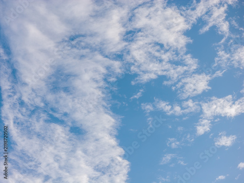 Broad white clouds on the left and smaller clusters on the right border a vertical corridor of clear blue sky. The open sky offers a calm backdrop featuring soft blue tones for a spacious composition.