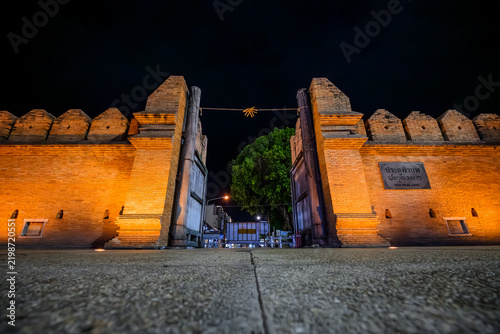 Historic Tha Phae Gate old red brick wall illuminated at night with warm golden lighting in the city center of Chiang Mai, Thailand