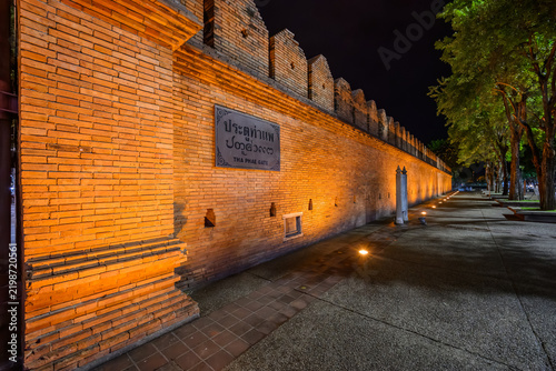 Historic Tha Phae Gate old red brick wall illuminated at night with warm golden lighting in the city center of Chiang Mai, Thailand