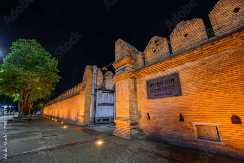 Historic Tha Phae Gate old red brick wall illuminated at night with warm golden lighting in the city center of Chiang Mai, Thailand