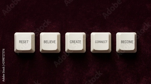 Inspirational words reset believe create connect and become printed on white computer keyboard keys over a dark background
