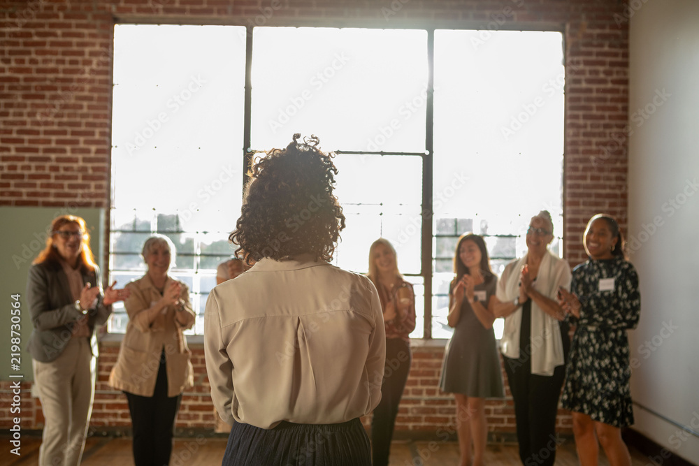 Fototapeta premium Group applauding a speaker in a sunlit brick-walled room.