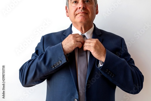 фотографія Man in a suit adjusting his tie against a white background.