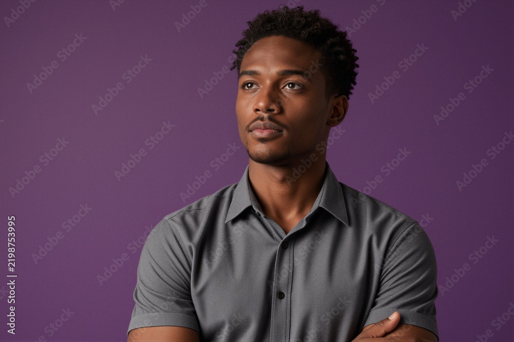 Fototapeta premium A man in a gray short-sleeved button-down shirt poses with arms crossed against a solid purple background.