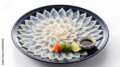Exquisite traditional Japanese fugu sashimi known as tessa meticulously arranged in a beautiful chrysanthemum pattern on an elegant dark plate served with savory ponzu sauce grated daikon and