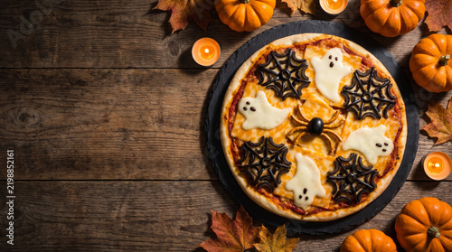 Spooky Halloween pizza flat lay with ghost and spiderweb topping creates playful seasonal scene on rustic wooden table