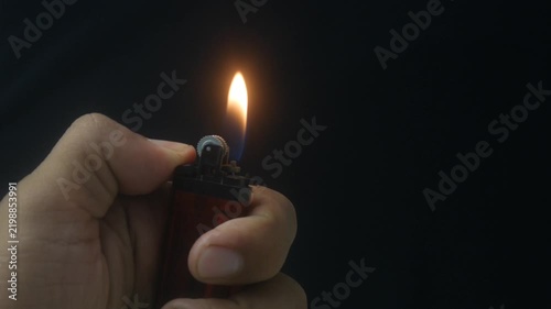 Hand holding a burning gas lighter with a small flame on a dark background