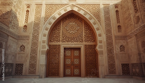 Intricate Islamic geometric carved stone archway with elegant wooden door in traditional courtyard.