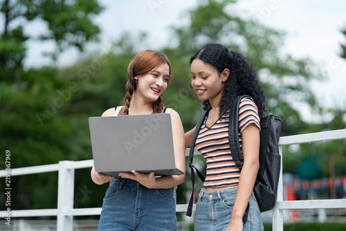 Asia and African American woman student college talking with notebook computer outdoor
