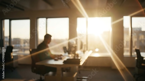 Silhouette of a dedicated professional working at desk inside modern corporate office during sunset with bright sun flares
