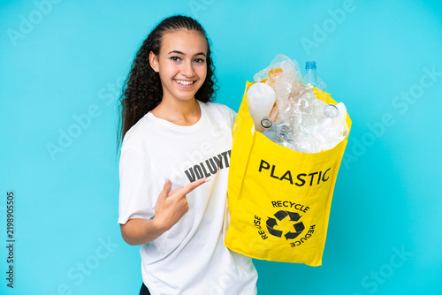 Foto Young woman holding a bag full of plastic bottles to recycle isolated on blue ba