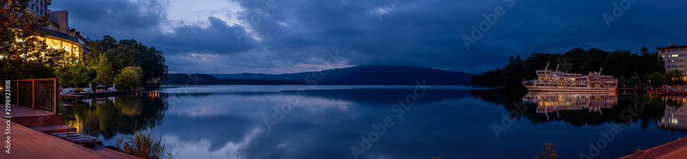 Obraz premium Panoramic view of Lake Akan at blue hour in Akankohan, Hokkaido, Japan, with mountains, lakeside buildings, boats, and reflections on the water.