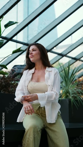Relaxed woman in casual clothes rolling up her sleeves while waiting on a bench