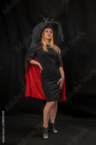 Obraz na płótnie Blonde woman wearing a black dress, a red lined black cape, and a witch hat with