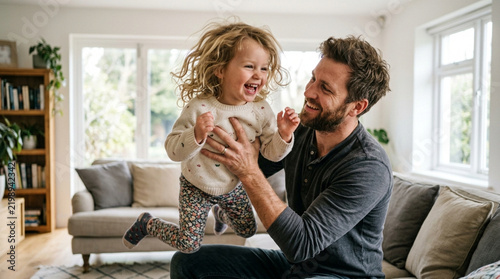 Father lifting happy laughing daughter in living room, joyful family moment