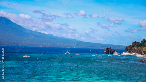 Clear blue sea water with boats and a distant island beneath a cloudy sky, a tranquil view seen from Apo island. Dauin, Negros Island Region, Philippines
