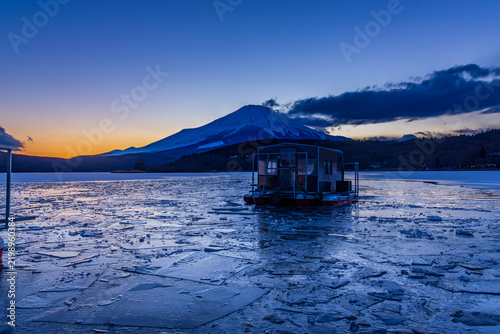 夕方の氷結した山中湖湖畔からブルーアワの富士山と帰船するワカサギ釣り船