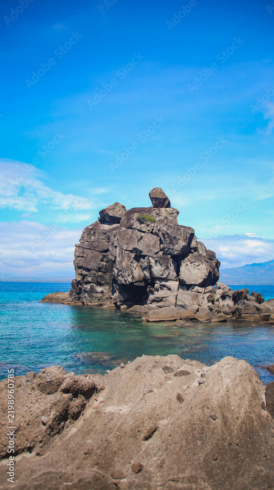 Obraz premium Vertical rock column formation called sea stack extending out of the water under a vivid blue sky. Apo Island, Philippines