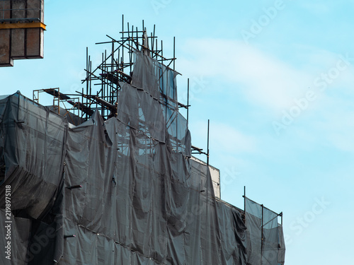 Obraz na plátne Building under construction wrapped in torn gray safety netting and steel scaffo