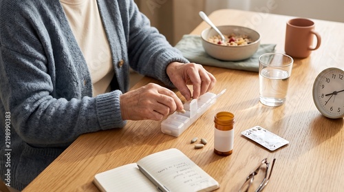 Senior woman organizing daily medication in a pill box at a wooden dining table