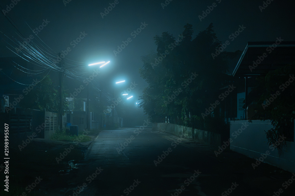 Fototapeta premium Misty empty neighborhood street illuminated by cold neon streetlights at dark quiet night.