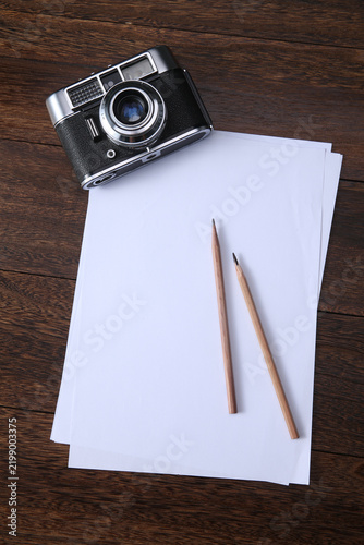 Foto Vintage Camera with Blank Paper and Pencils on Wood Desktop