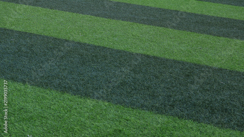 Картината върху платно Close up texture of a two-tone green striped artificial turf football field back