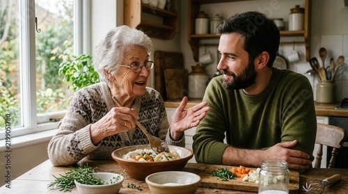 Senior grandmother and adult grandson cooking and talking happily at home kitchen table
