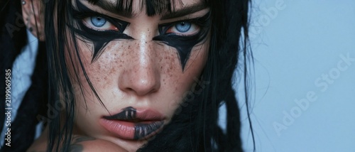 Freckled woman with striking blue eyes and angular black eye makeup in a dramatic close-up leaving generous pale blue negative space Concept of bold beauty