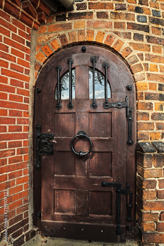 Arched wooden door with heavy historic iron fittings and ring handle in the brickwork of the Schrotturm city wall tower, photographed in portrait format.