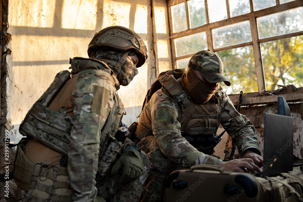 Obraz premium Soldiers operate a drone control console. Military personnel are carrying out a combat mission at a position in an abandoned house.