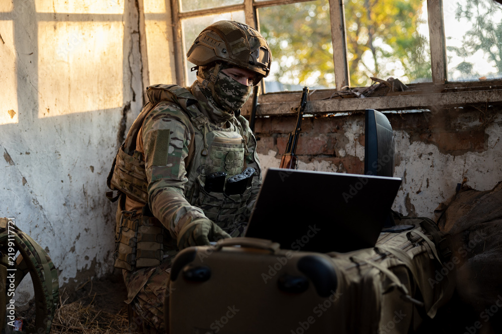 Obraz premium Soldier operates a drone control console. Military personnel is carrying out a combat mission at a position in an abandoned house.