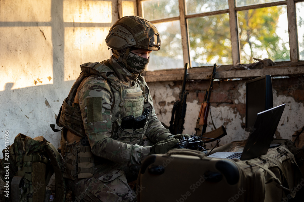 Obraz premium Soldier operates a drone control console. Military personnel is carrying out a combat mission at a position in an abandoned house.