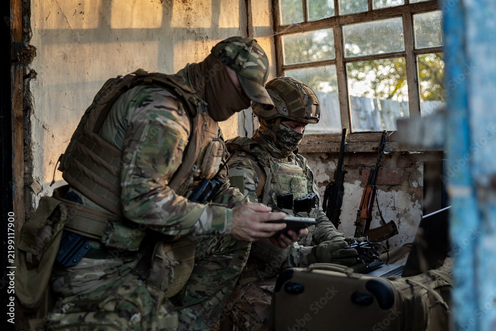 Obraz premium Soldiers operate a drone control console. Military personnel are carrying out a combat mission at a position in an abandoned house.