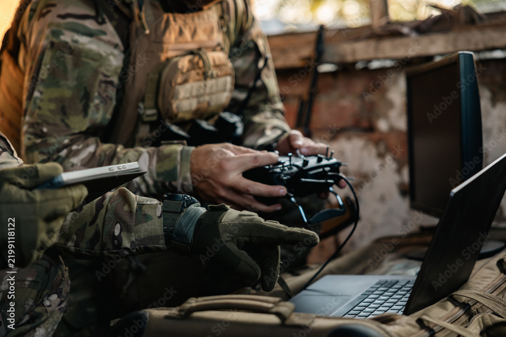 Obraz premium Soldier operates a drone control console. Military personnel is carrying out a combat mission at a position in an abandoned house.
