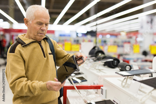 elderly man examines tablet computer in showroom of electronics store