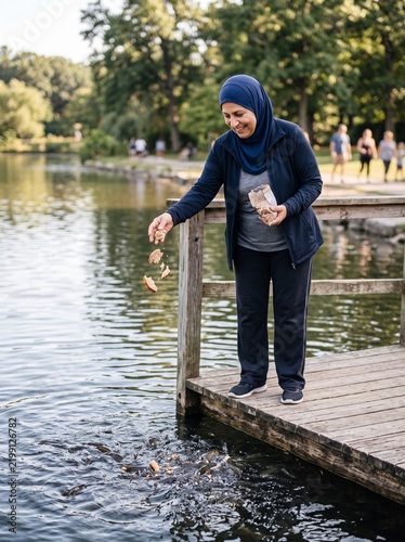 Woman tossing pieces of bread to school of fish