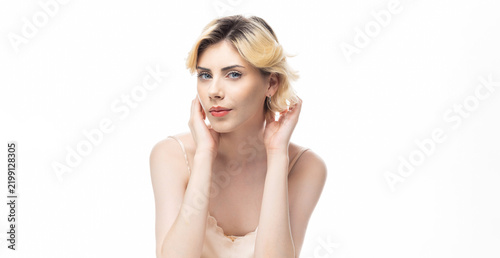 A young blonde girl with clear skin in a satin top. Beauty portrait of a woman on a white background in the studio.