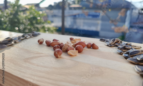 Horizontal eye-level macro perspective of grouped peanuts flanked by sunflower seeds on a light wooden plank surface with an out-of-focus background