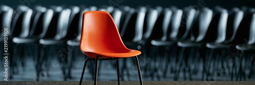 Orange chair standing out from black chairs. Orange chair representing individuality and uniqueness in a row of many identical black chairs