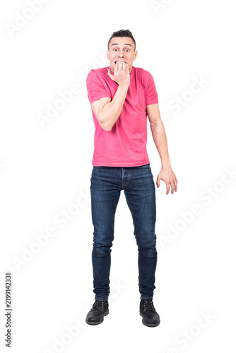 Full body of young nervous male with dark hair in t shirt and jeans biting nails and looking at camera