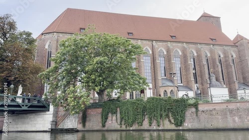 Scenic view of a historic red brick gothic church on the Odra riverbank in Wroclaw, Poland. Beautiful summer European travel destination for cultural tourism and outdoor sightseeing.   