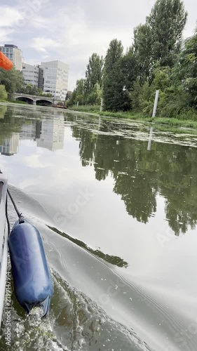 POV from a tourist boat with a blue fender showing the reflection of a modern glass office building on the Odra river in Wroclaw, Poland. Beautiful summer travel lifestyle and urban sightseeing.