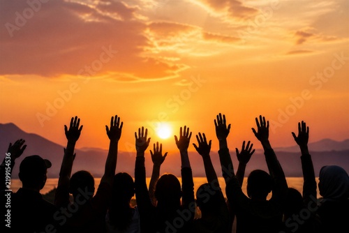 Group raising hands toward sunset over lake shore horizon