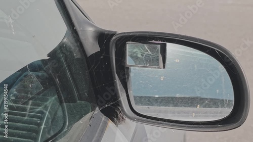 Detail shot of a dusty, spiderweb covered car side view mirror. The reflection shows the road as another vehicle overtakes it